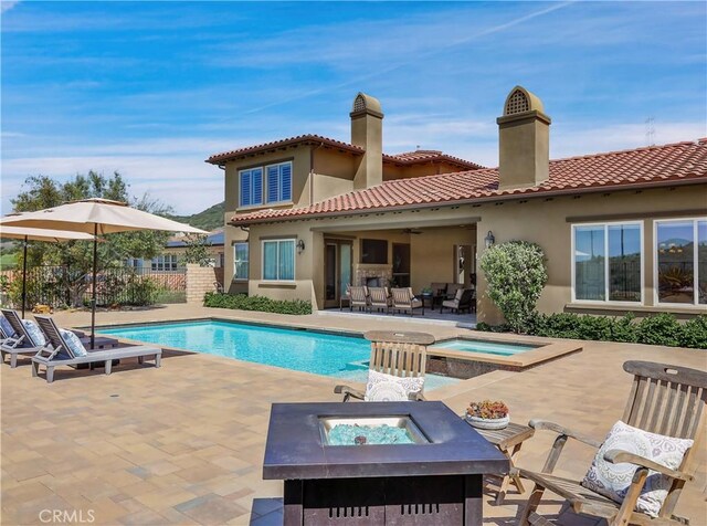 rear view of house with a tiled roof, an in ground hot tub, a chimney, a patio area, and a fenced in pool