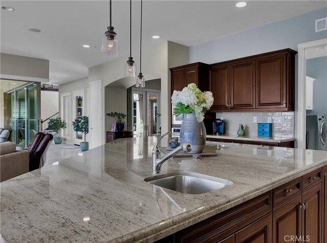 kitchen with tasteful backsplash, light stone countertops, a sink, open floor plan, and separate washer and dryer