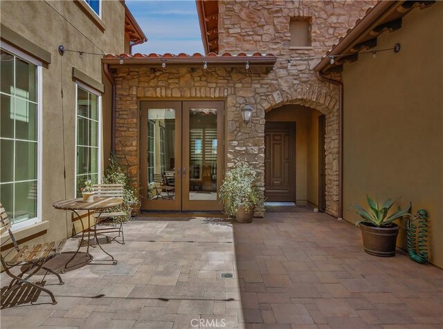 view of exterior entry with a patio, stucco siding, french doors, and stone siding