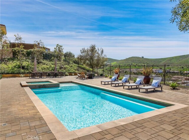view of swimming pool featuring a patio area, a mountain view, a pool with connected hot tub, and fence