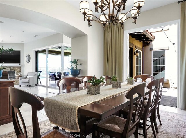 dining space with arched walkways, an inviting chandelier, light tile patterned floors, and a fireplace