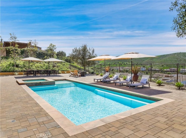 view of swimming pool with fence, a patio, a pool with connected hot tub, and outdoor dining space