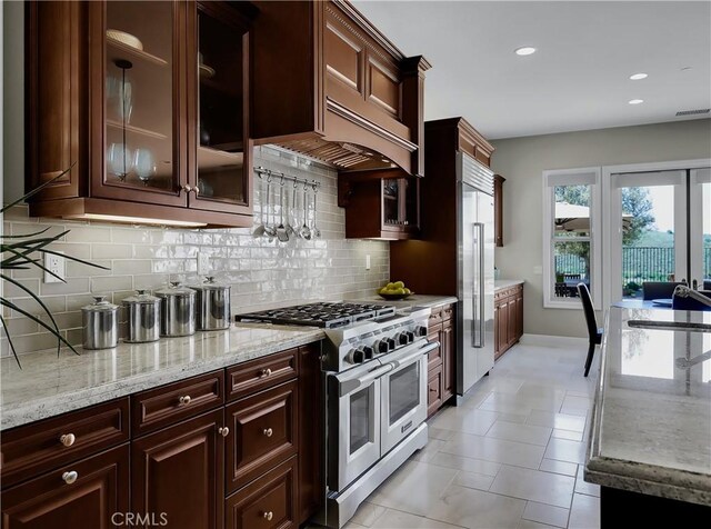 kitchen with premium appliances, light stone countertops, glass insert cabinets, and tasteful backsplash