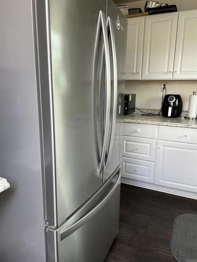 kitchen featuring light stone counters, dark wood-style floors, white cabinets, and freestanding refrigerator