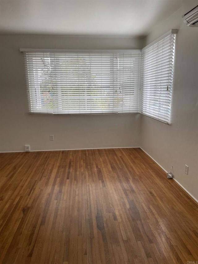 spare room featuring plenty of natural light, a wall unit AC, and wood-type flooring