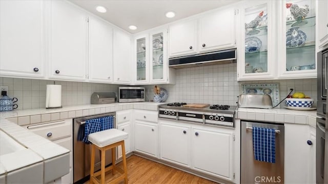 kitchen featuring under cabinet range hood, appliances with stainless steel finishes, white cabinetry, and tile counters