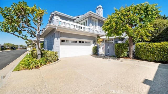 view of front of property featuring a balcony, fence, an attached garage, a chimney, and concrete driveway