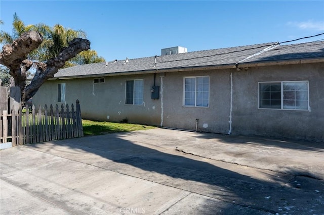 rear view of house with stucco siding, roof with shingles, and fence