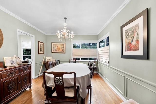 dining room featuring light wood finished floors, a healthy amount of sunlight, crown molding, and an inviting chandelier