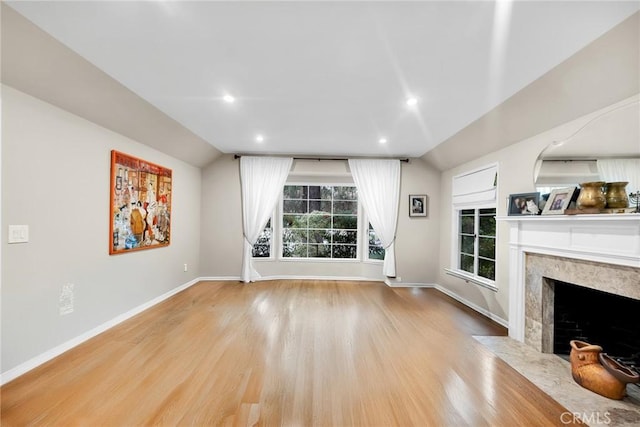 unfurnished living room with baseboards, a premium fireplace, vaulted ceiling, recessed lighting, and wood finished floors