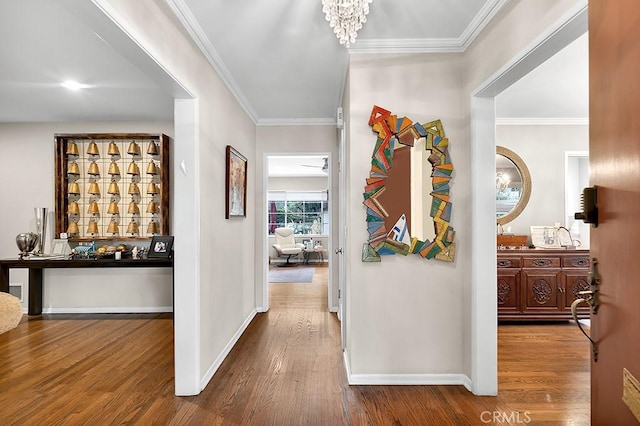 hallway featuring a chandelier, crown molding, baseboards, and wood finished floors