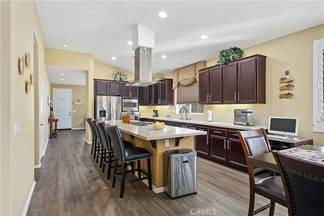 kitchen with dark wood-style floors, stainless steel appliances, a breakfast bar area, island range hood, and light countertops