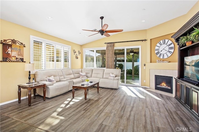 living area featuring baseboards, a tiled fireplace, lofted ceiling, wood finished floors, and a ceiling fan