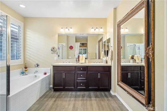 full bath with double vanity, wood finished floors, a garden tub, and a sink