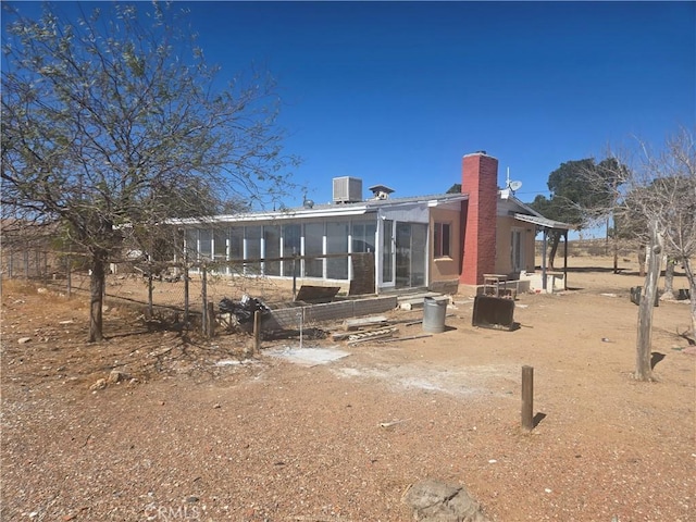 rear view of property with central AC unit, a chimney, and a sunroom