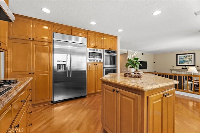 kitchen featuring light stone counters, light wood finished floors, a kitchen island, built in appliances, and brown cabinets