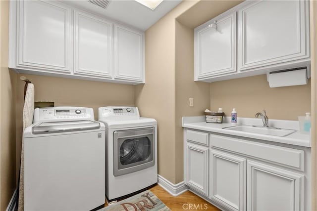 laundry area featuring baseboards, washing machine and clothes dryer, cabinet space, a sink, and light wood-style floors