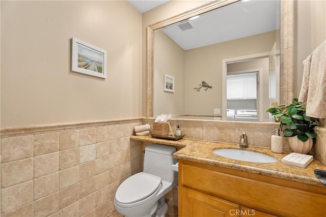 bathroom featuring vanity, visible vents, wainscoting, tile walls, and toilet