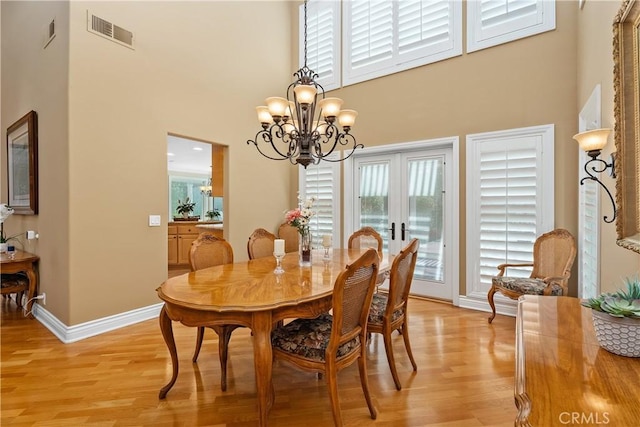 dining space featuring visible vents, baseboards, light wood-style floors, a towering ceiling, and a notable chandelier