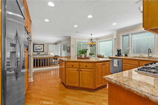 kitchen featuring ornamental molding, a kitchen island, stainless steel appliances, light wood-style floors, and a chandelier