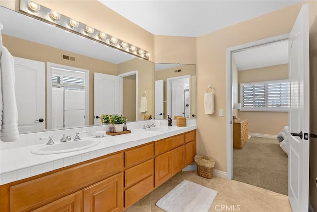 ensuite bathroom featuring a sink, visible vents, baseboards, and double vanity