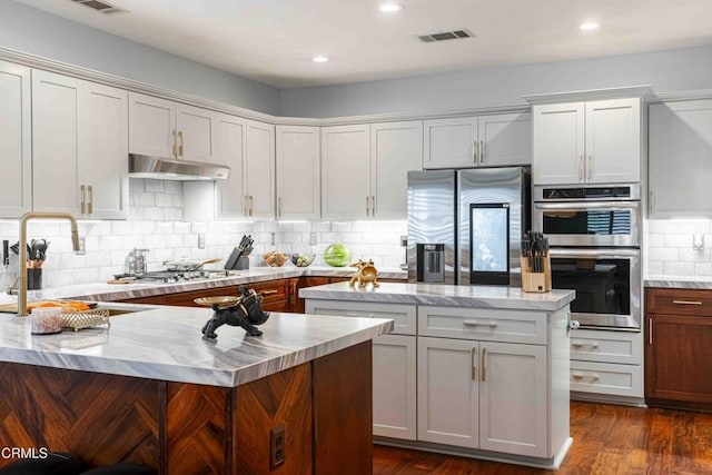 kitchen featuring visible vents, a center island, under cabinet range hood, dark wood finished floors, and stainless steel appliances