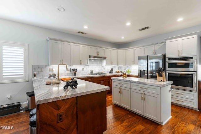 kitchen featuring visible vents, a peninsula, stainless steel appliances, and dark wood-style flooring