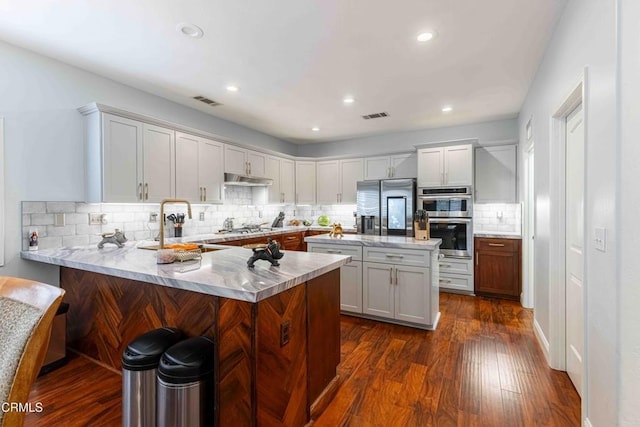 kitchen featuring visible vents, dark wood-type flooring, appliances with stainless steel finishes, a peninsula, and light countertops