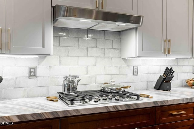 kitchen featuring decorative backsplash, stainless steel gas stovetop, under cabinet range hood, and butcher block counters