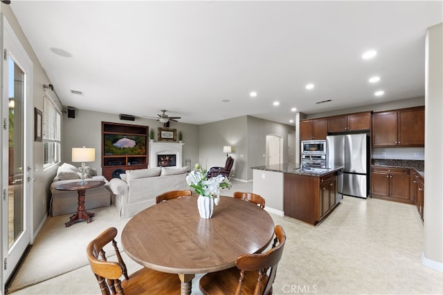 dining room featuring visible vents, baseboards, ceiling fan, a lit fireplace, and recessed lighting