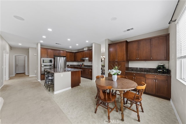 kitchen featuring visible vents, under cabinet range hood, a sink, stainless steel appliances, and a breakfast bar area