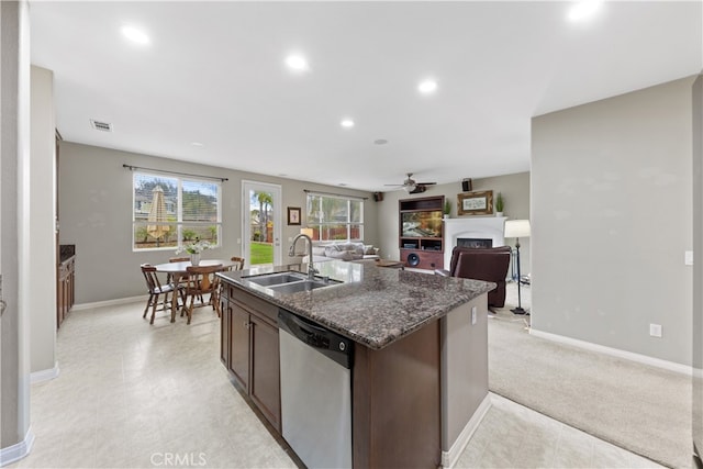 kitchen with an island with sink, a sink, stainless steel dishwasher, a fireplace, and dark brown cabinets