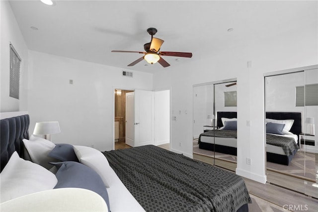 bedroom featuring a ceiling fan, wood finished floors, visible vents, baseboards, and two closets