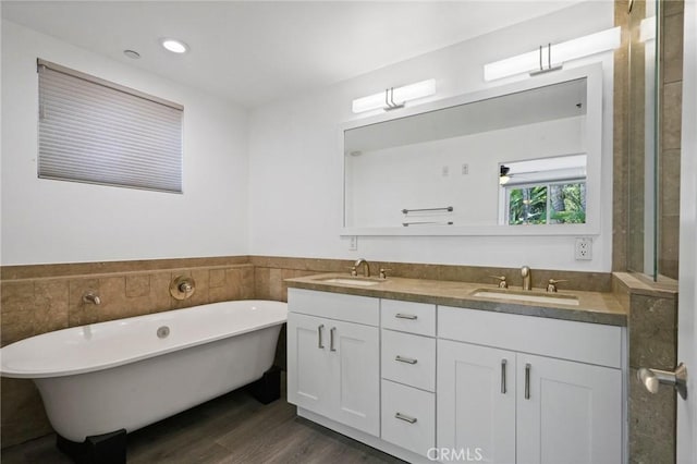 bathroom featuring a sink, a freestanding tub, wood finished floors, and double vanity