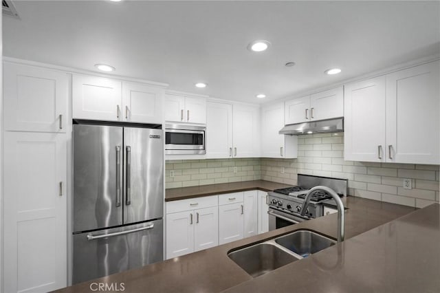 kitchen featuring white cabinetry, dark countertops, premium appliances, and under cabinet range hood