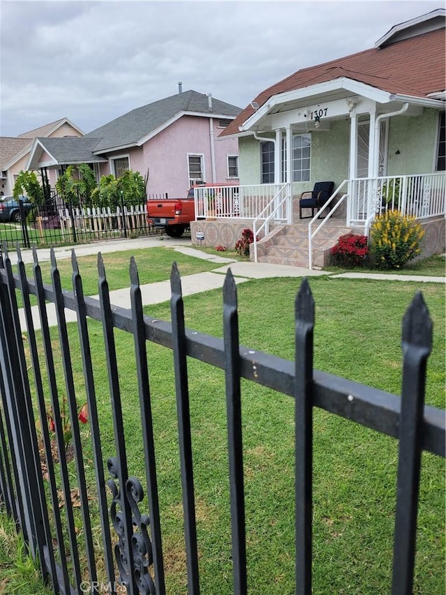 view of front facade with stucco siding, a porch, a front lawn, and fence