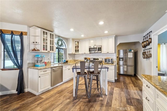 kitchen with a sink, stainless steel appliances, dark wood finished floors, and white cabinetry