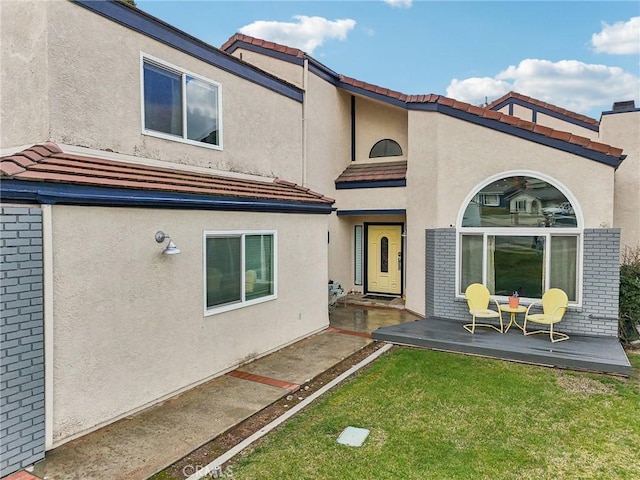 rear view of property with a patio, a tiled roof, a yard, and stucco siding