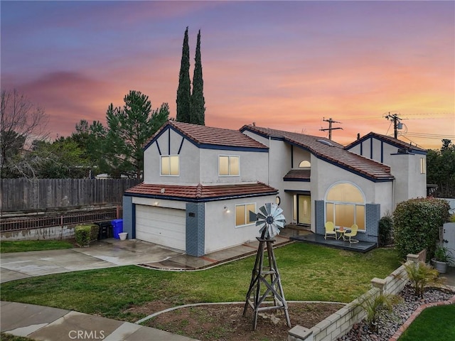 back of property at dusk featuring a lawn, driveway, a tile roof, fence, and an attached garage