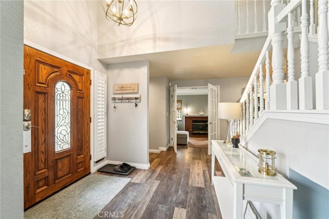 foyer entrance featuring a notable chandelier, wood finished floors, baseboards, a brick fireplace, and stairs