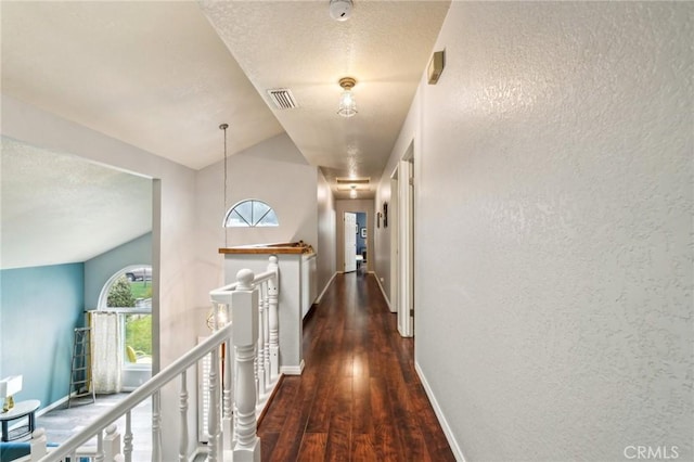 corridor with visible vents, an upstairs landing, a textured ceiling, wood finished floors, and baseboards