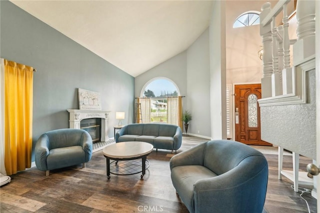 living room featuring a glass covered fireplace, baseboards, high vaulted ceiling, and wood finished floors