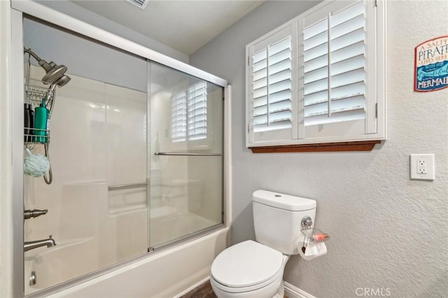 full bathroom featuring toilet, a textured wall, and combined bath / shower with glass door