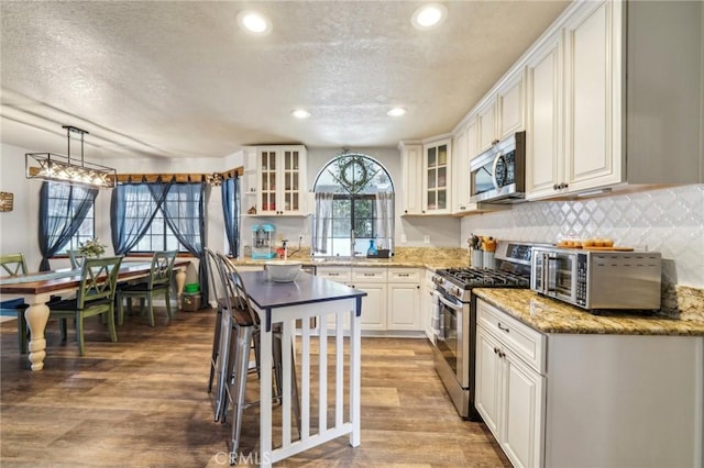 kitchen featuring appliances with stainless steel finishes, white cabinetry, glass insert cabinets, and light wood-style floors