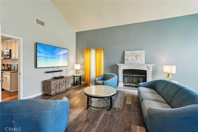 living room featuring visible vents, high vaulted ceiling, a glass covered fireplace, wood finished floors, and baseboards