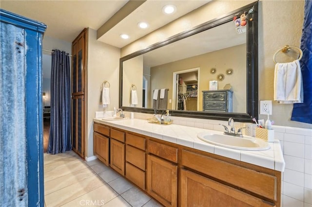 bathroom featuring tile patterned flooring, a walk in closet, double vanity, and a sink