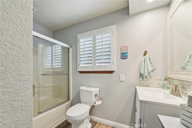 bathroom with baseboards, bath / shower combo with glass door, toilet, wood finished floors, and vanity