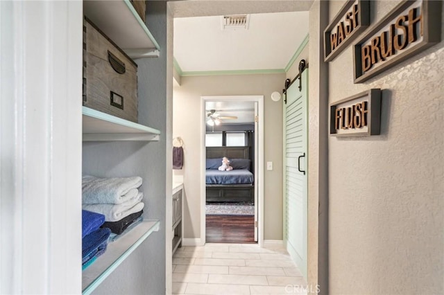 hallway with tile patterned flooring, visible vents, baseboards, a barn door, and ornamental molding