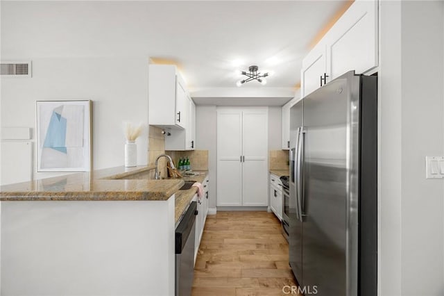 kitchen featuring visible vents, light wood-style flooring, white cabinetry, stainless steel appliances, and decorative backsplash