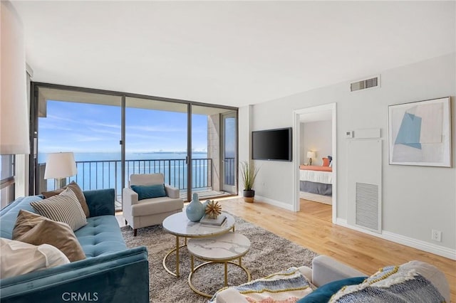 living room featuring a wall of windows, visible vents, baseboards, and wood finished floors